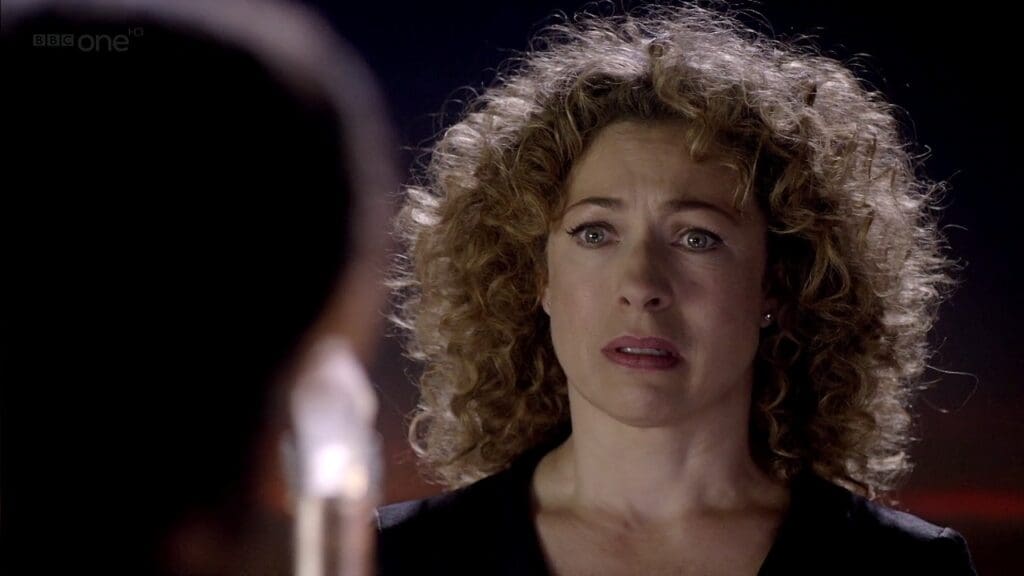 River Song, looking at the Doctor, teary eyed.