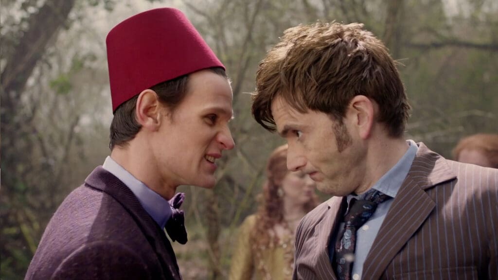 The Eleventh Doctor, wearing a fez, pulls a face at the Tenth