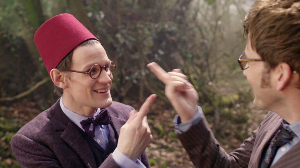 The Tenth and Eleventh Doctor are both wearing glasses, pointing at each other