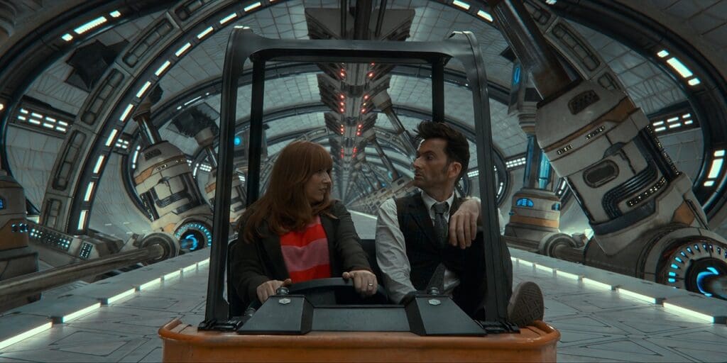 Donna driving the Doctor in a golf cart along a giant space corridor