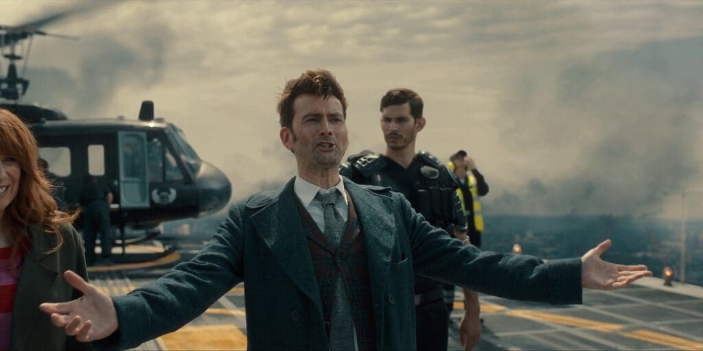 The 14th Doctor with his arms wide open. He is on the UNIT HQ helipad.