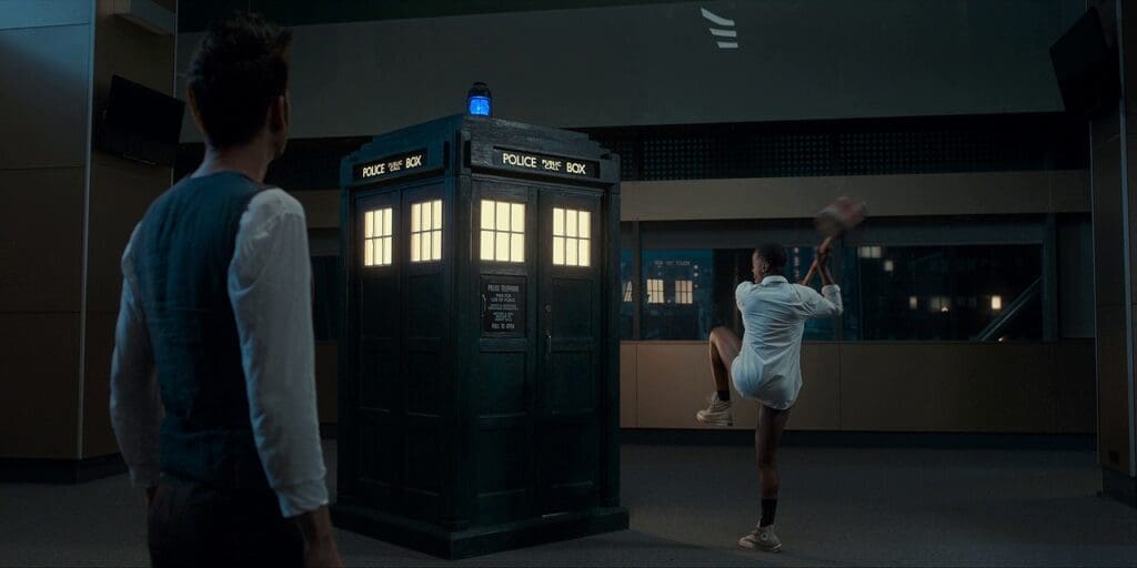 The 15th Doctor swinging a giant comedy carnival mallet at the TARDIS,