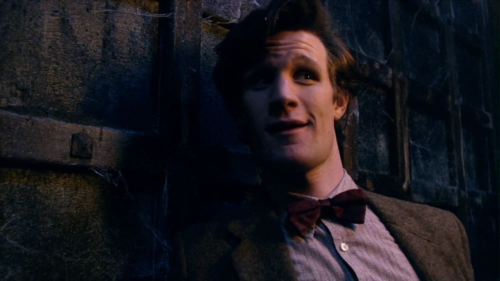 The Doctor, leaning up against the Pandorica, smiling