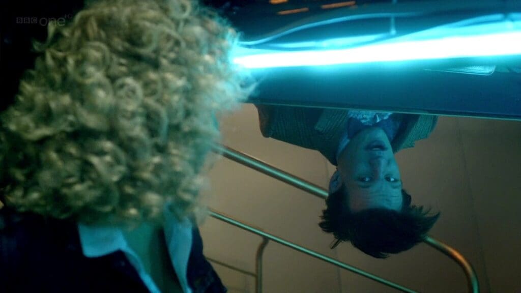 The Doctor is upside down looking at River in the TARDIS