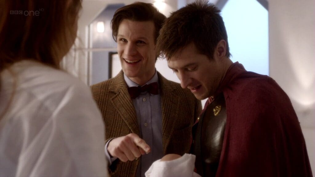 Rory is holding Melody, The Doctor is pointing at her