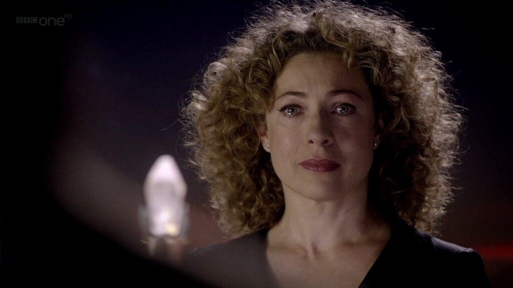 River Song, looking at the Doctor, teary eyed.