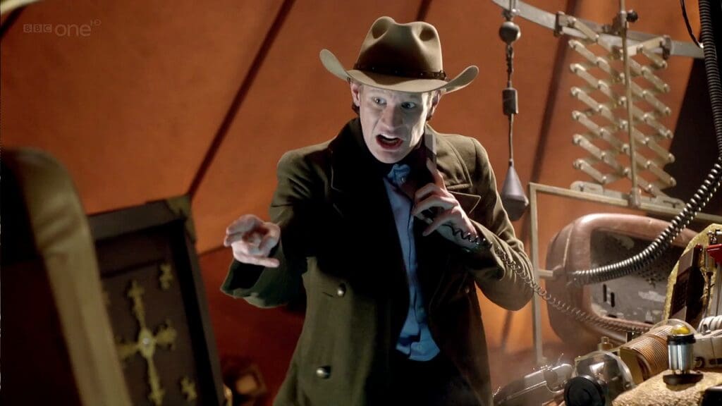 The Doctor in the TARDIS, wearing a Stetson and on the phone, gesticulating as he talks to Dorium.